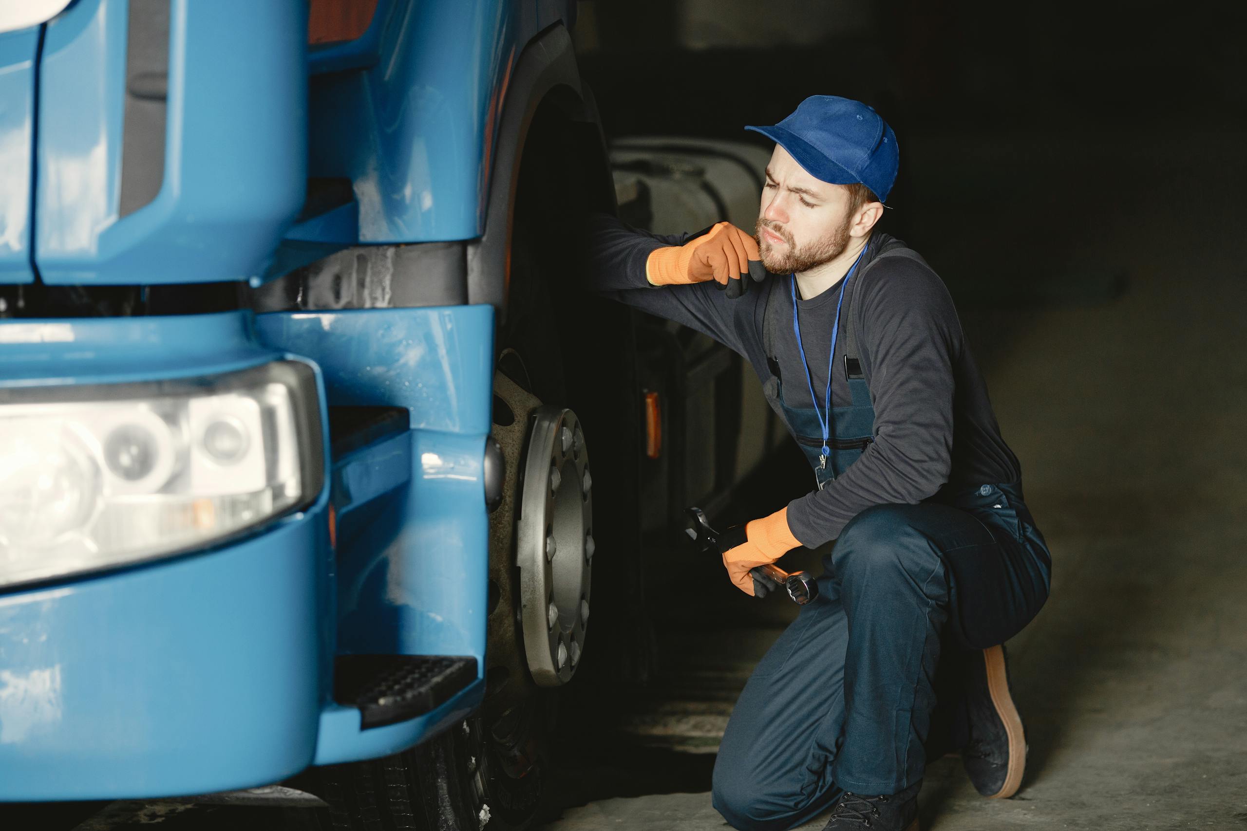 Pensive mechanic examining a truck wheel for maintenance in an indoor garage setting.